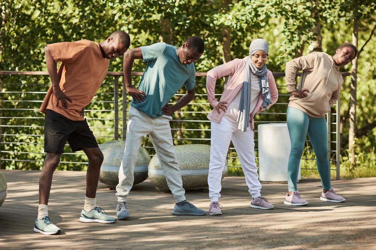Four adults stretch together outdoors in a park.