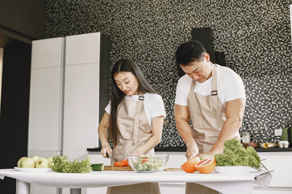 Two adults prepare a healthy meal with fresh vegetables at home.