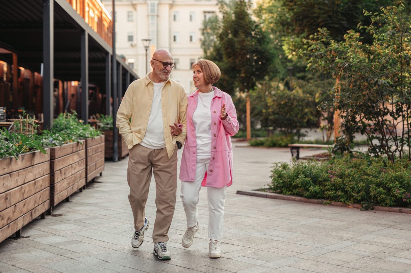 An older couple walks together through a garden.